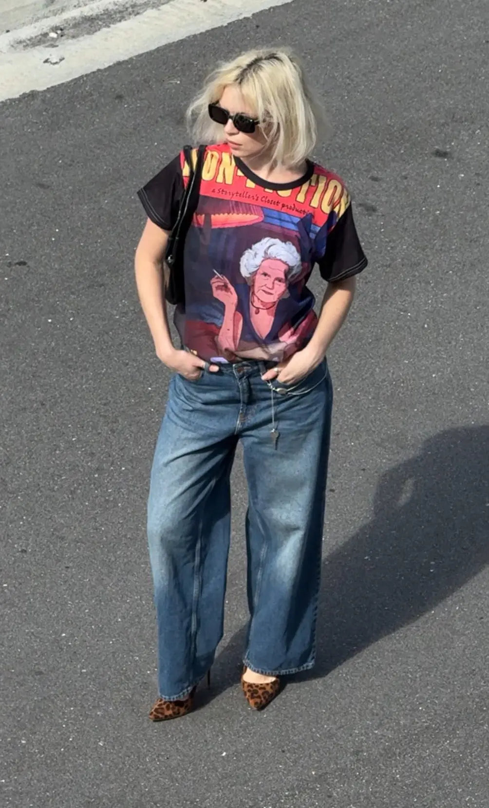 Person wearing a graphic t-shirt and blue jeans standing on a paved surface.