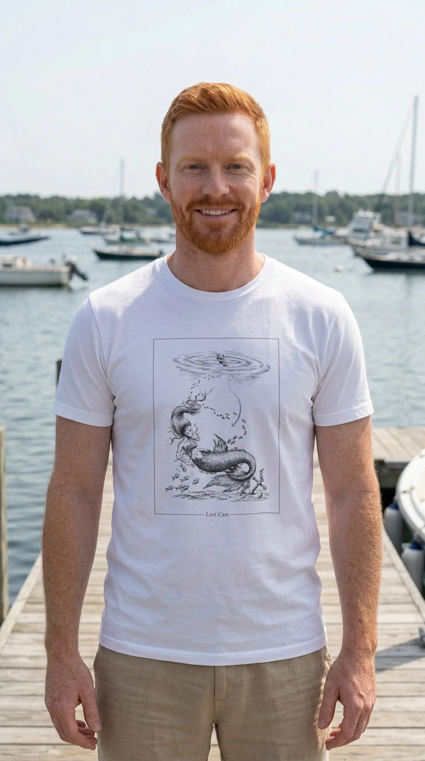 Man wearing a white t-shirt with a graphic design standing on a dock by a body of water.