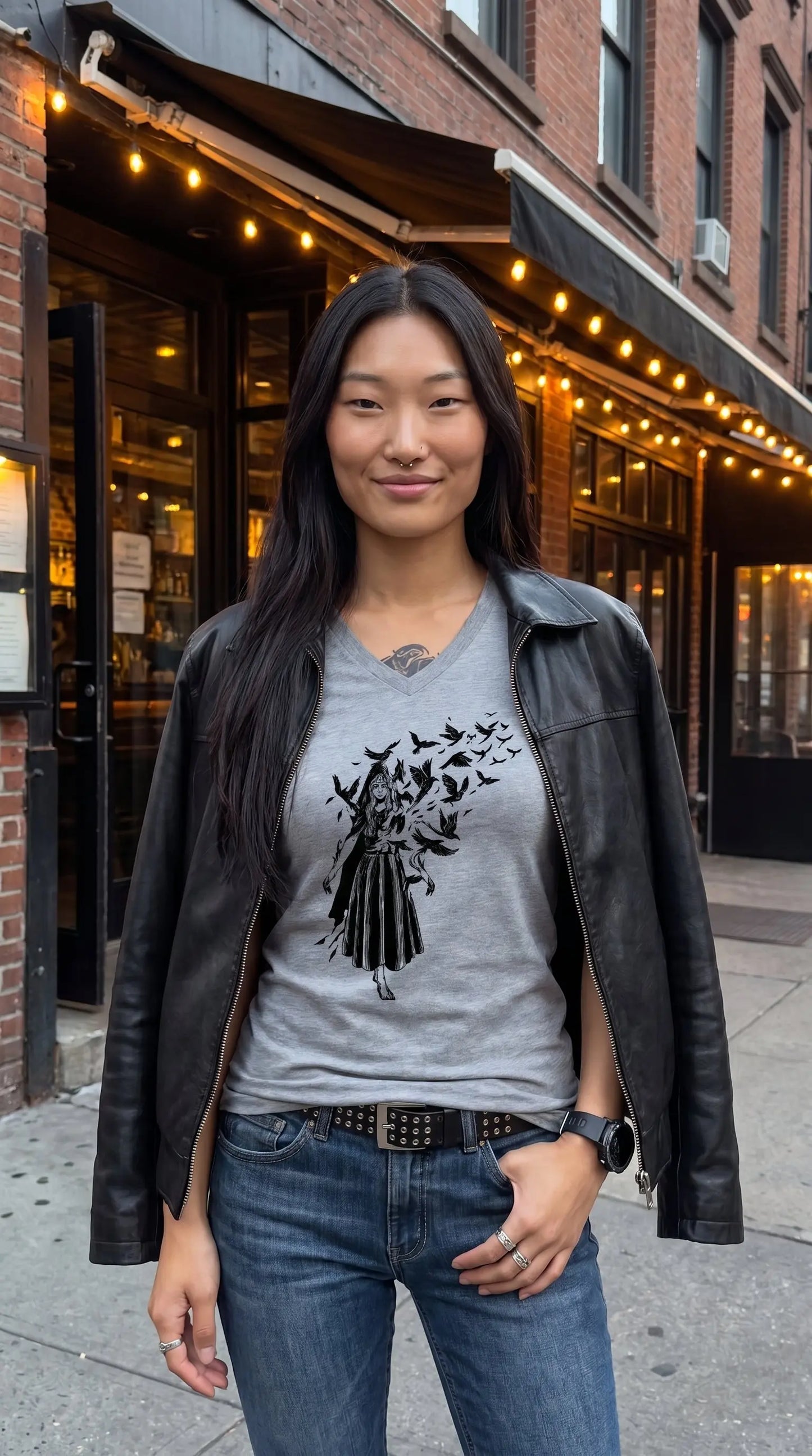 Woman wearing a gray t-shirt with a black graphic design, standing on a street with a building in the background.