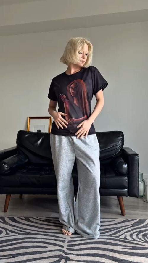 Load image 1 in gallery view. Person wearing a Storyteller's Closet Grace t-shirt with a graphic design and gray pants in a living room.