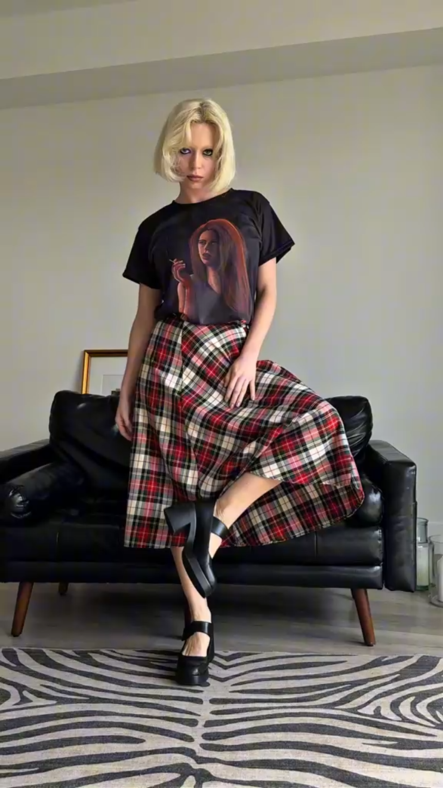 Person wearing Storyteller's Closet Grace t-shirt with a graphic design and a plaid skirt sitting.